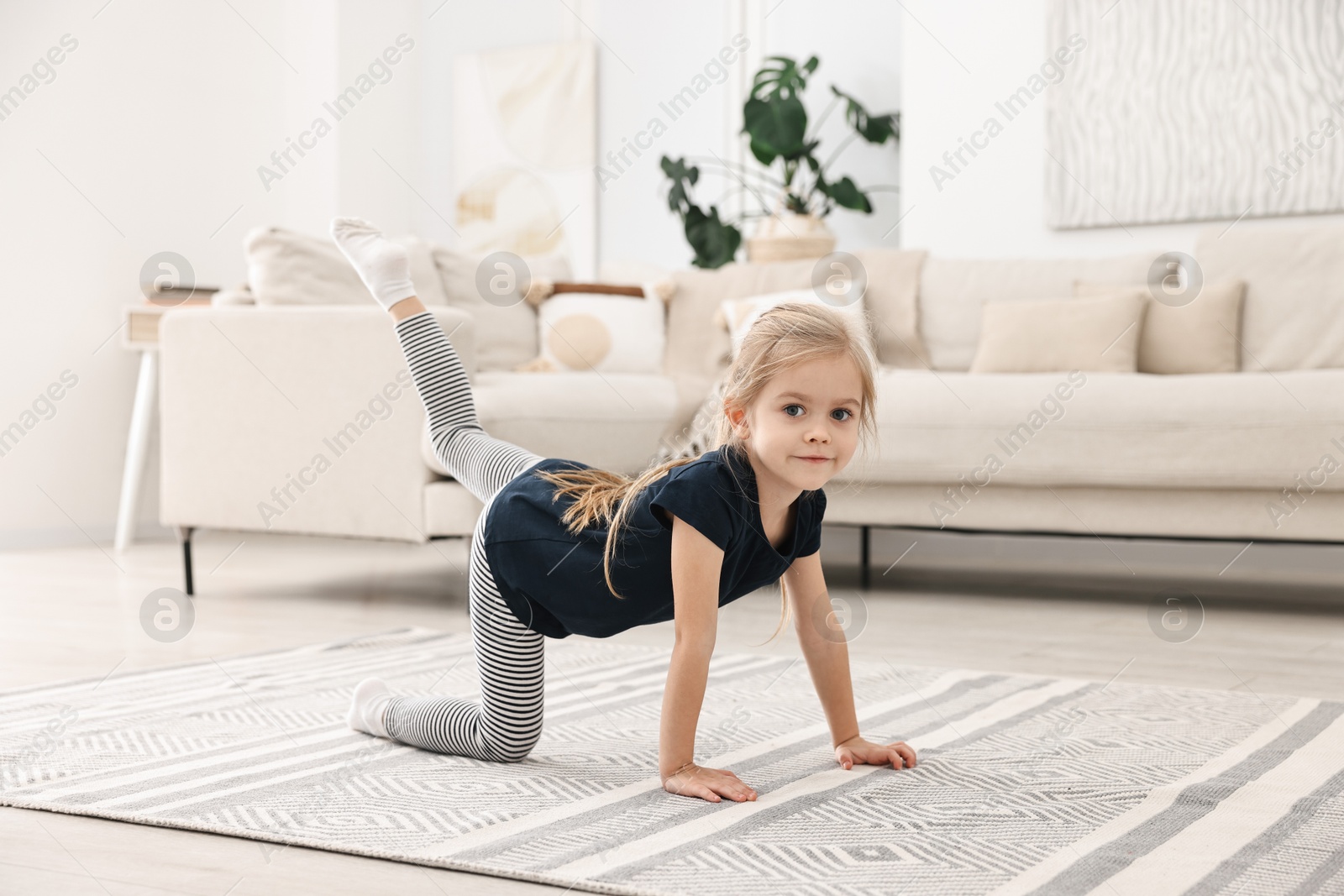 Photo of Little girl exercising on rug at home. Sport activity