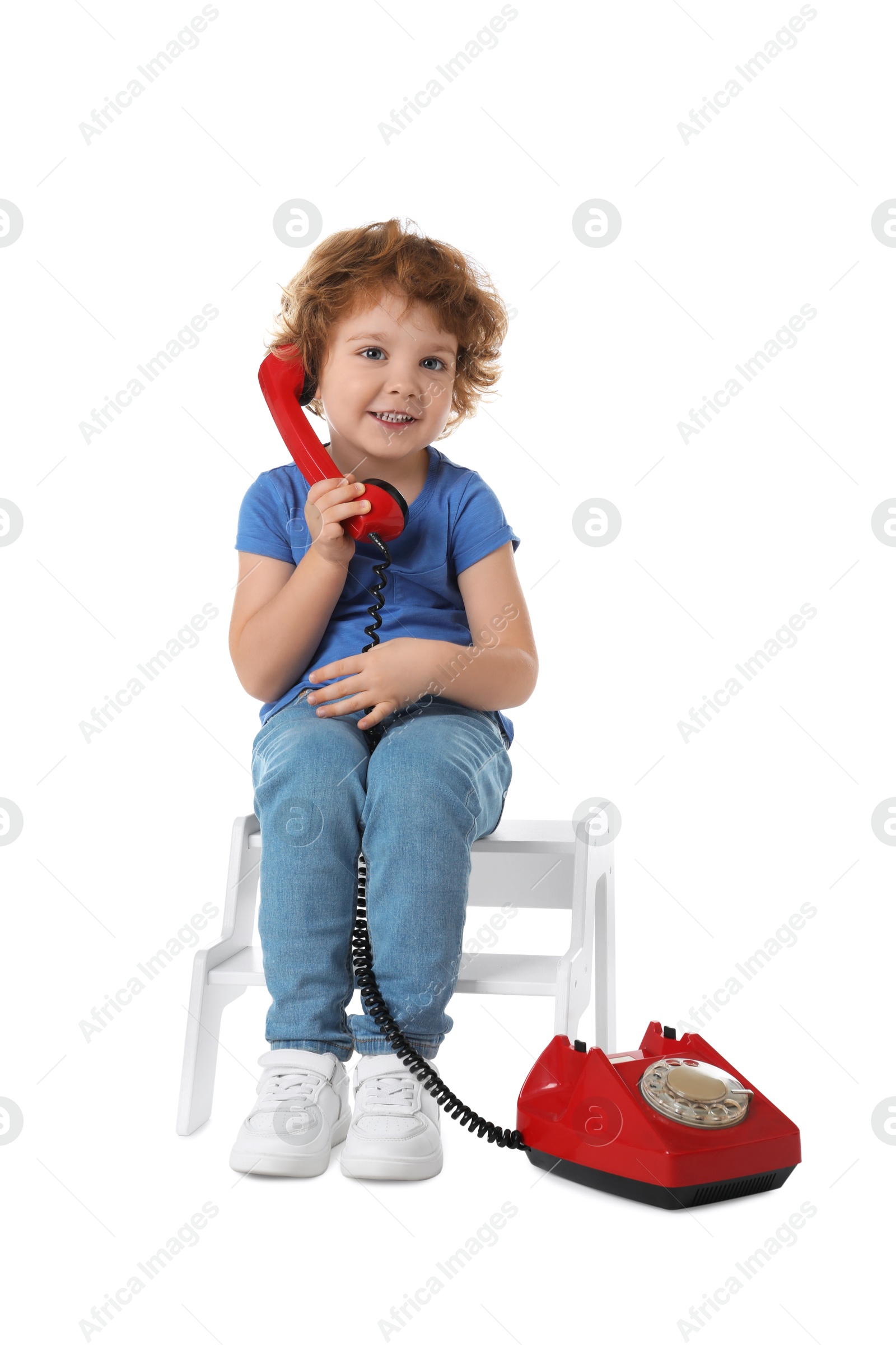 Photo of Cute little boy with telephone on step stool against white background