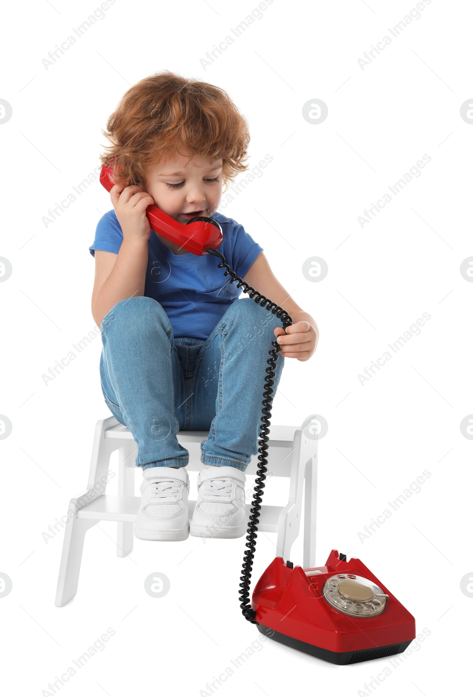 Photo of Cute little boy with telephone on step stool against white background