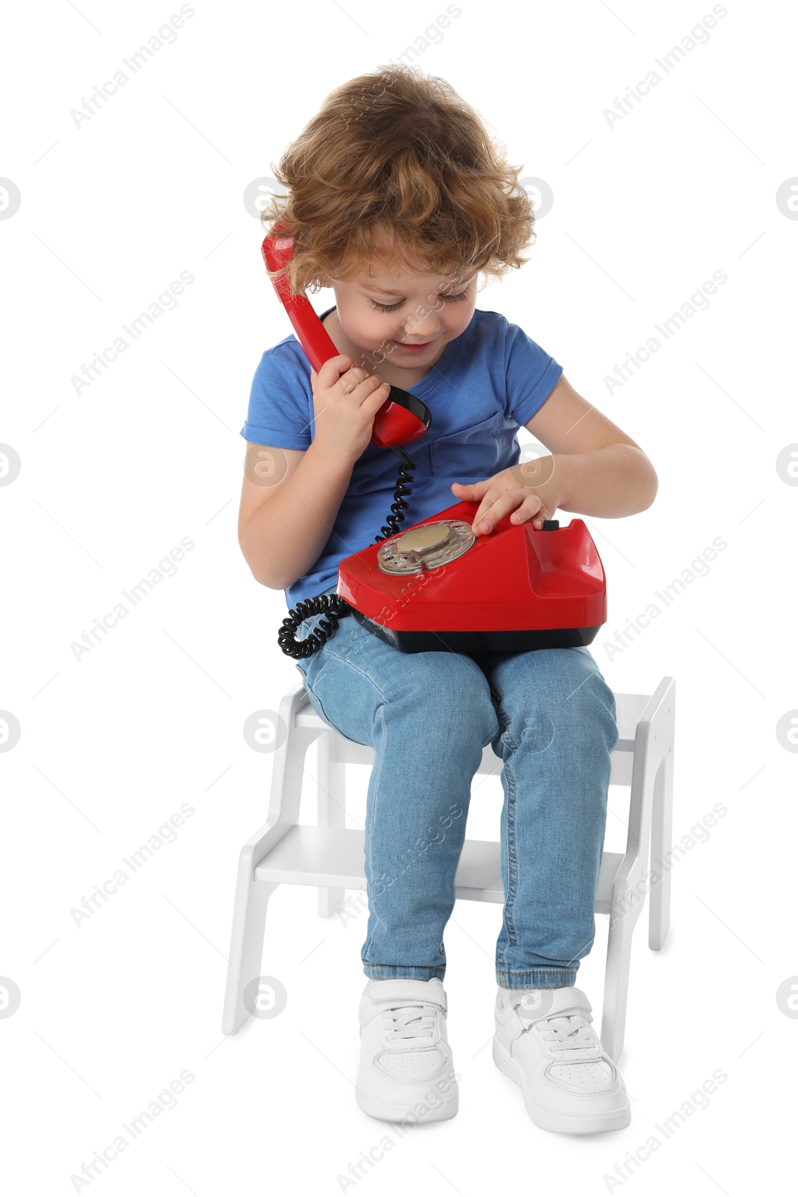 Photo of Cute little boy with telephone on step stool against white background