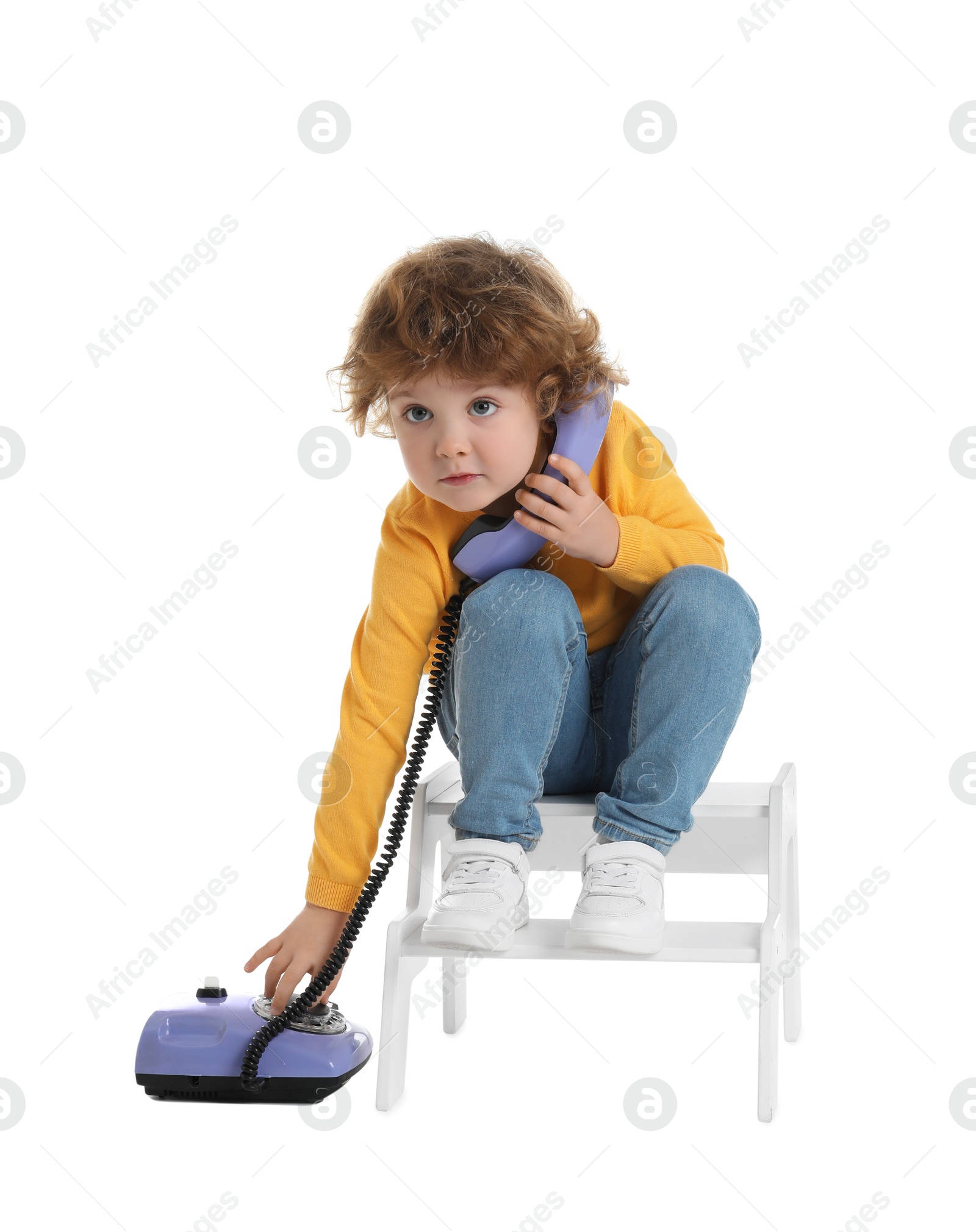 Photo of Cute little boy with telephone on step stool against white background