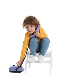 Photo of Cute little boy with telephone on step stool against white background