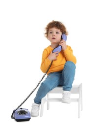 Photo of Cute little boy with telephone on step stool against white background