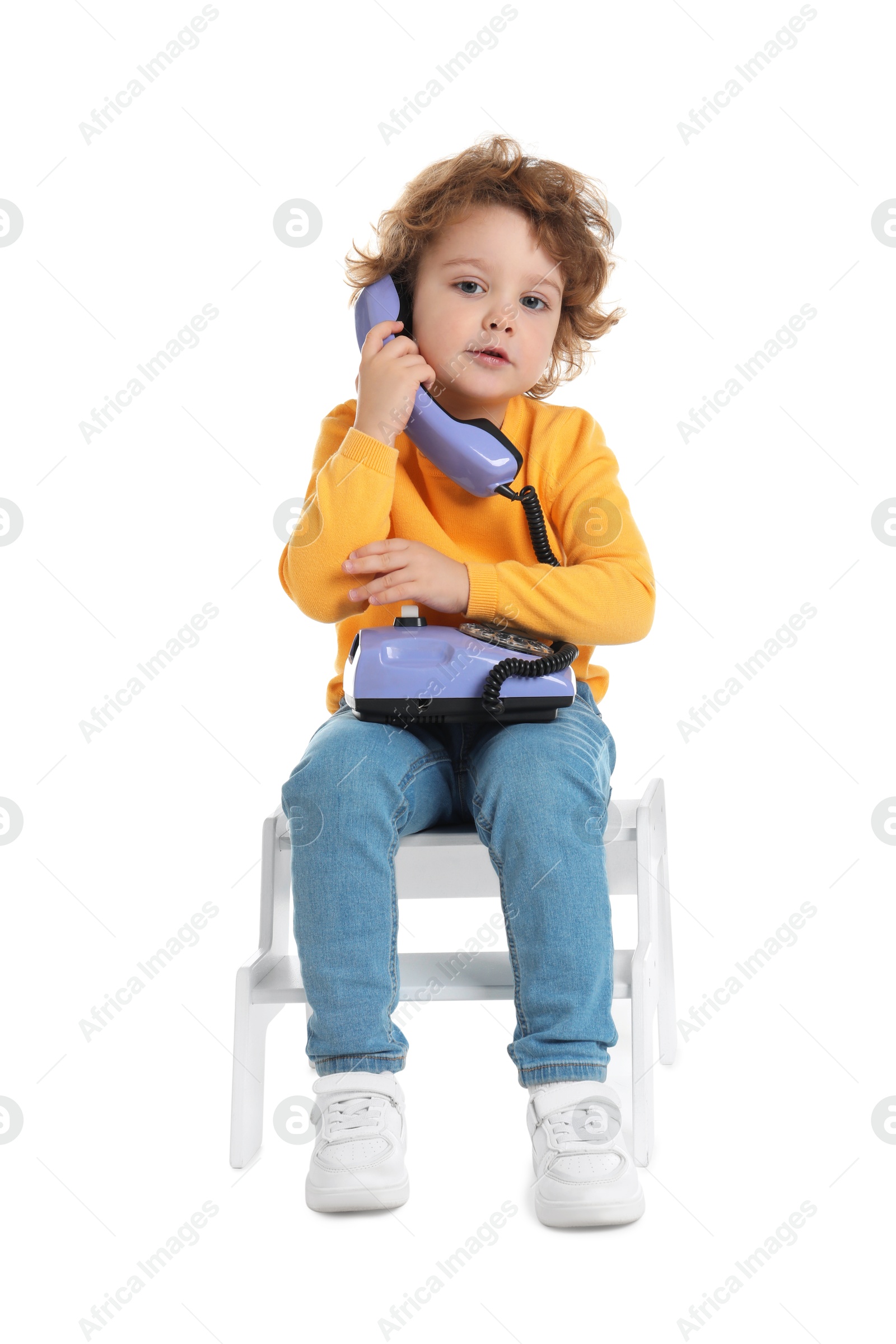 Photo of Cute little boy with telephone on step stool against white background