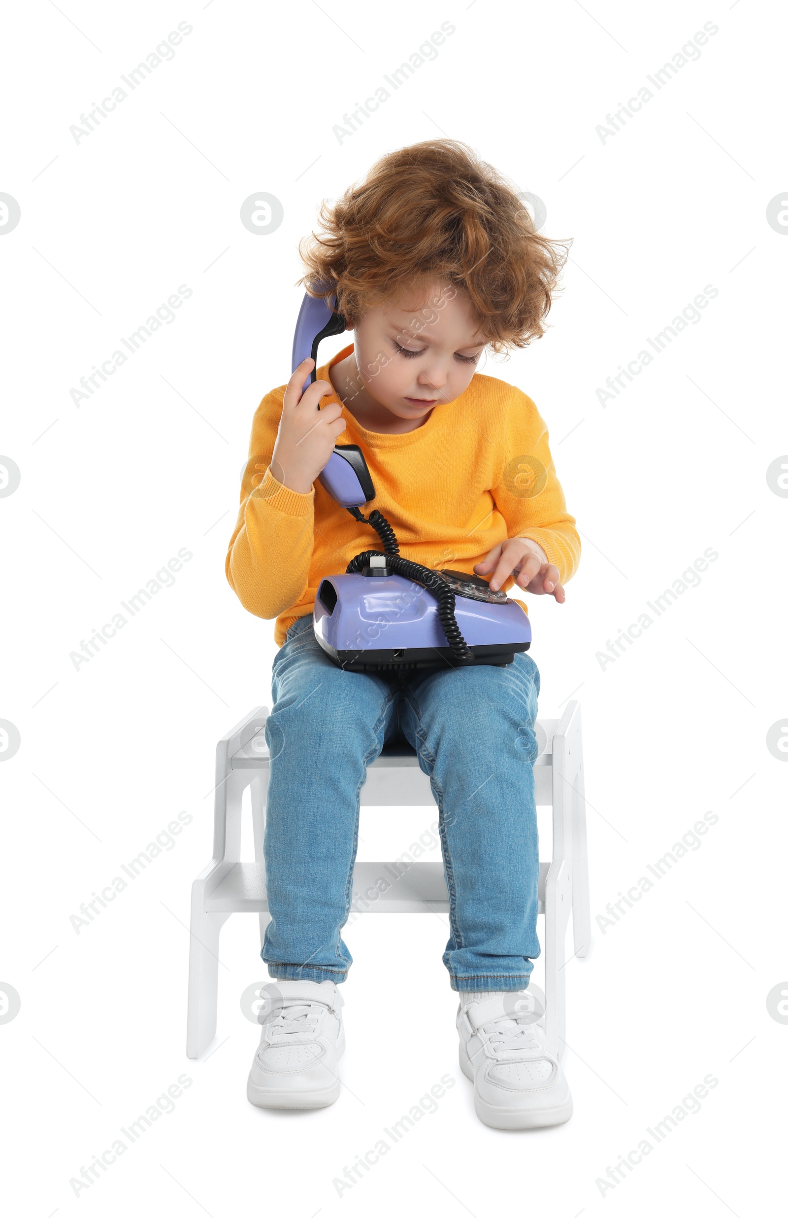 Photo of Cute little boy with telephone on step stool against white background