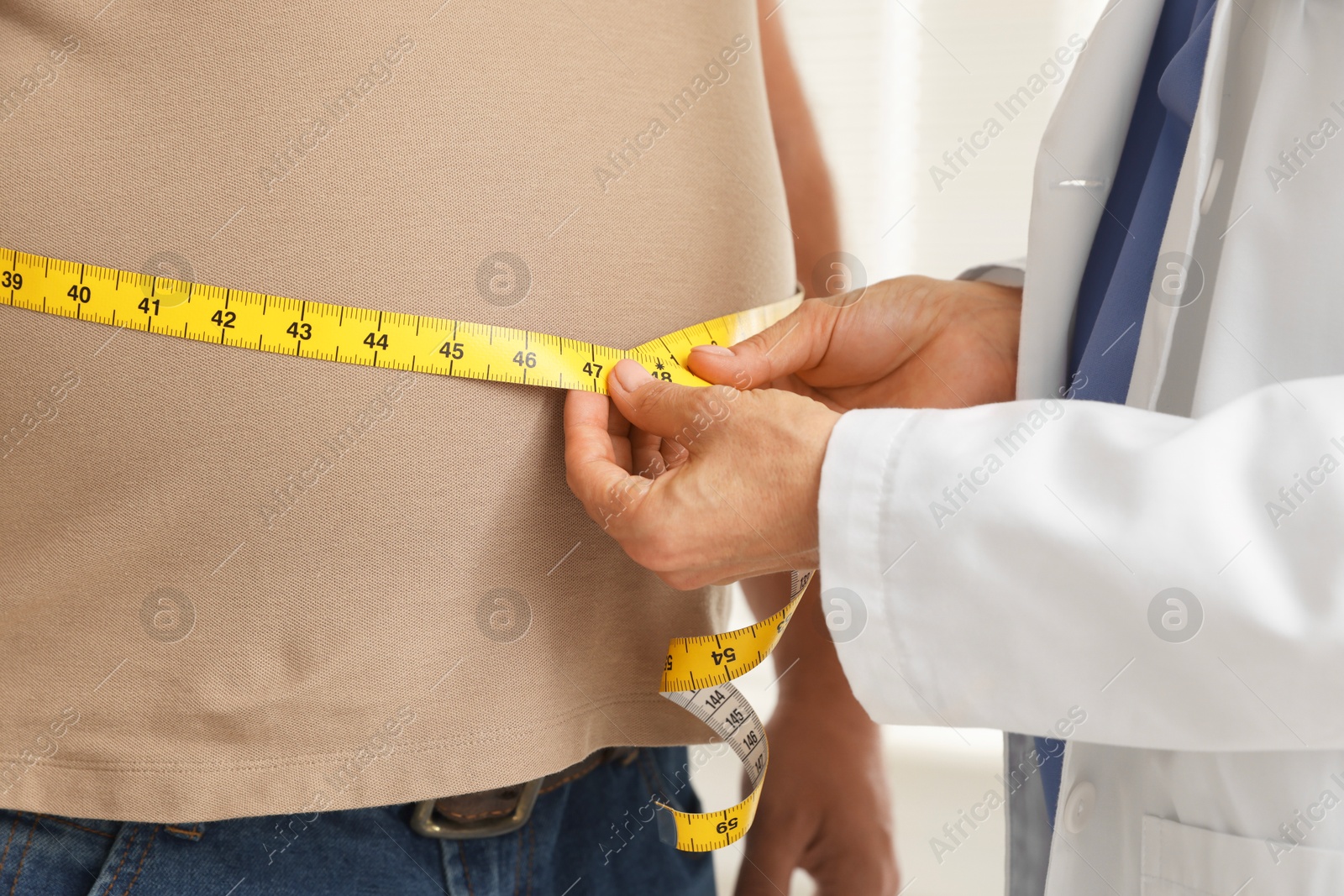 Photo of Nutritionist measuring overweight man's waist with tape in clinic, closeup