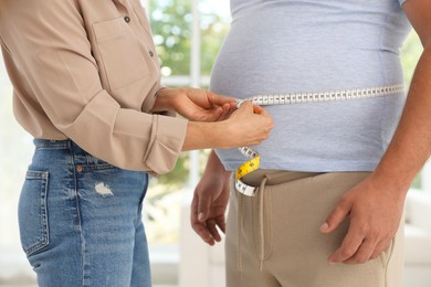 Photo of Nutritionist measuring overweight man's waist with tape in clinic, closeup