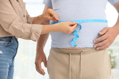 Photo of Nutritionist measuring overweight man's waist with tape in clinic, closeup