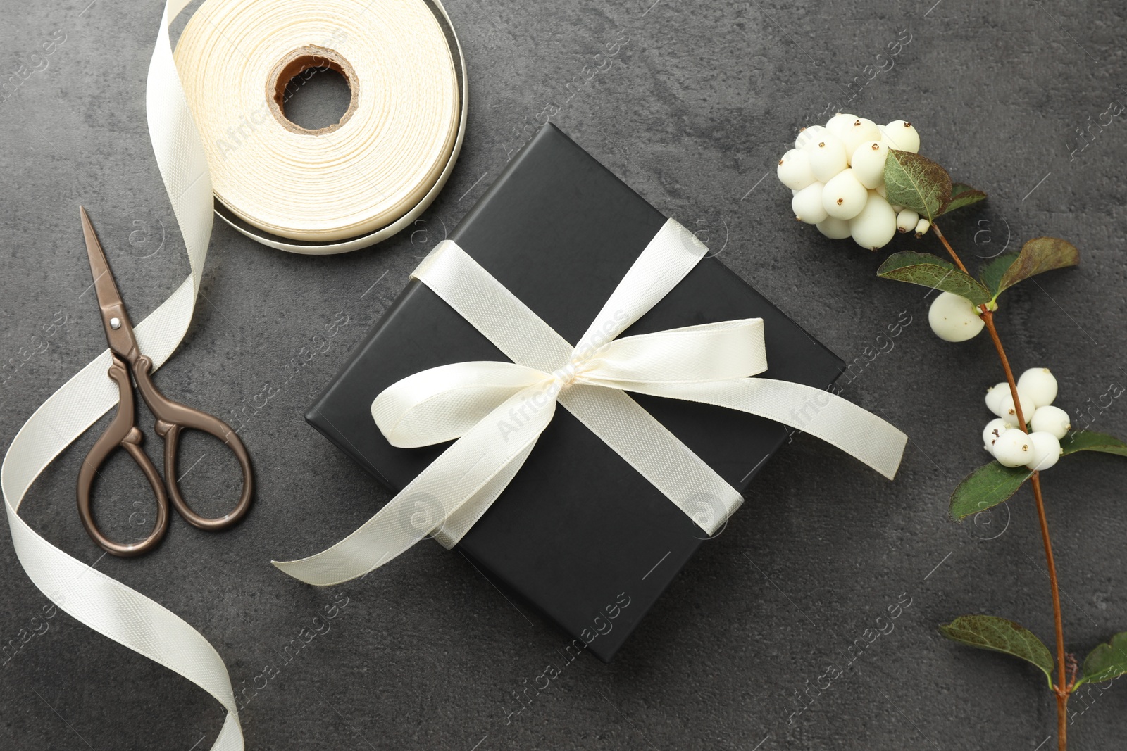 Photo of Gift box with bow, ribbon, scissors and flowers on grey table, flat lay