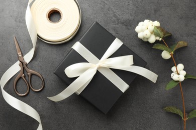 Gift box with bow, ribbon, scissors and flowers on grey table, flat lay