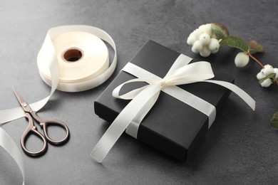 Gift box with bow, ribbon, scissors and flowers on grey table