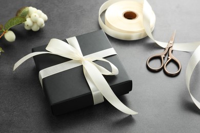 Photo of Gift box with bow, ribbon, scissors and flowers on grey table