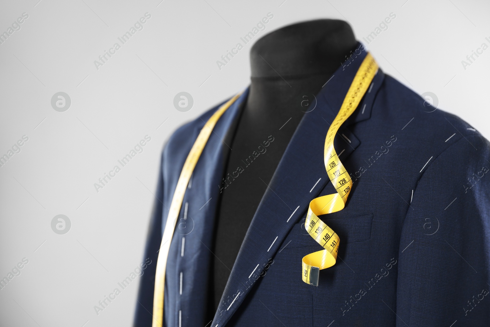 Photo of Semi-ready jacket and measuring tape on mannequin against gray background, closeup. Space for text