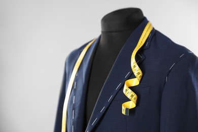 Photo of Semi-ready jacket and measuring tape on mannequin against gray background, closeup. Space for text