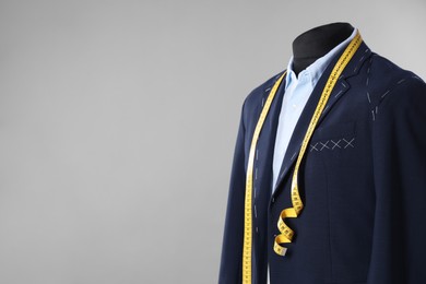 Photo of Semi-ready jacket, shirt and measuring tape on mannequin against gray background, closeup. Space for text