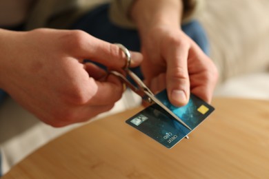 Photo of Man cutting credit card at wooden table indoors, closeup