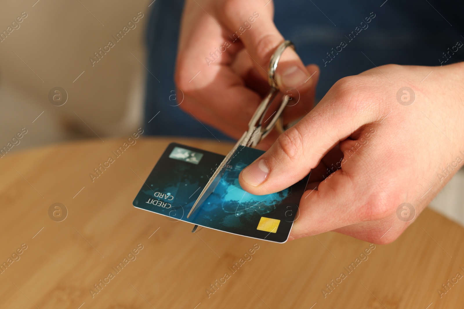 Photo of Man cutting credit card at wooden table indoors, closeup