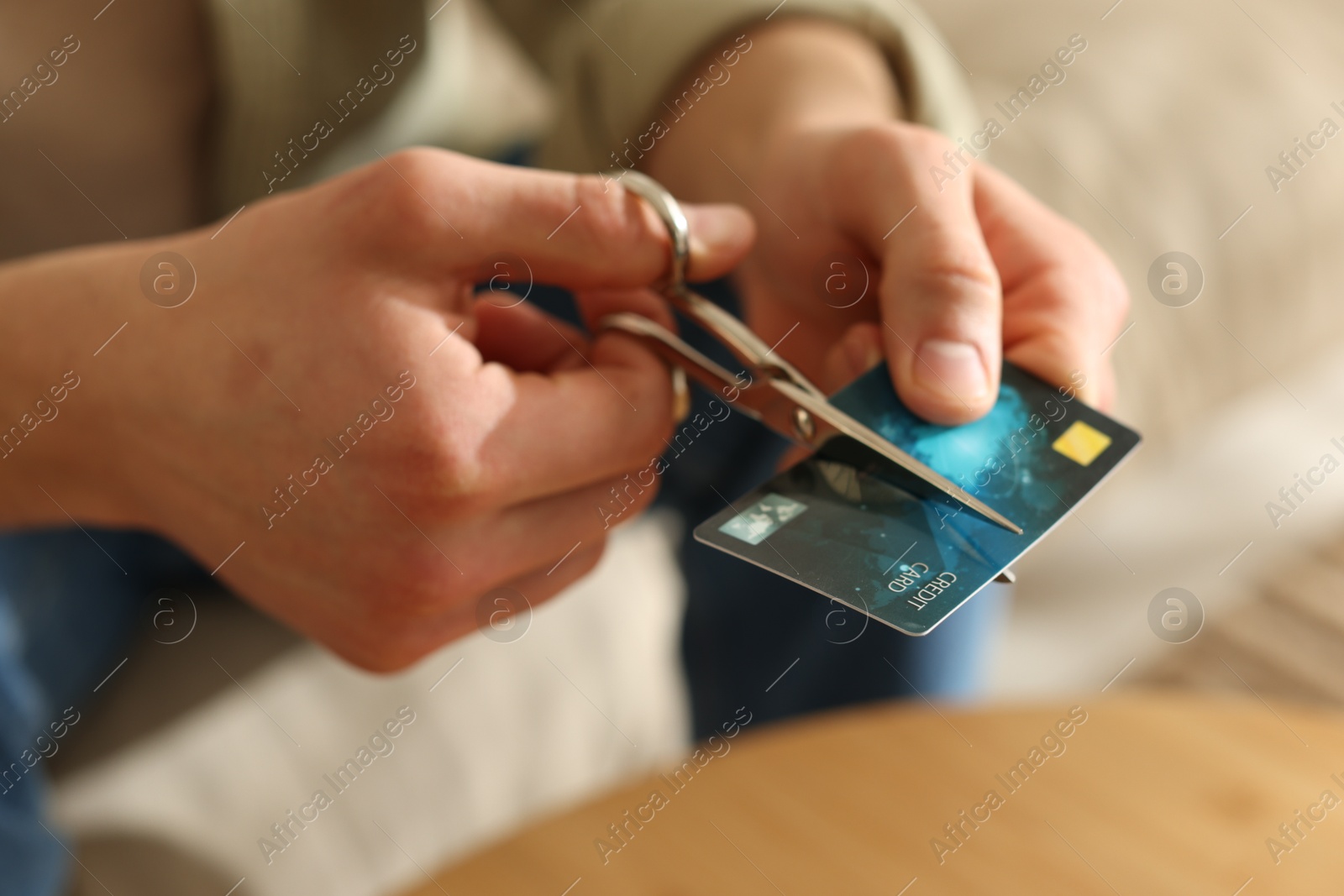 Photo of Man cutting credit card at wooden table indoors, closeup