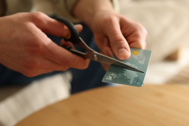 Photo of Man cutting credit card at wooden table indoors, closeup