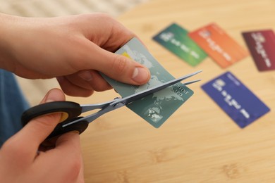 Photo of Man cutting credit card at wooden table indoors, closeup