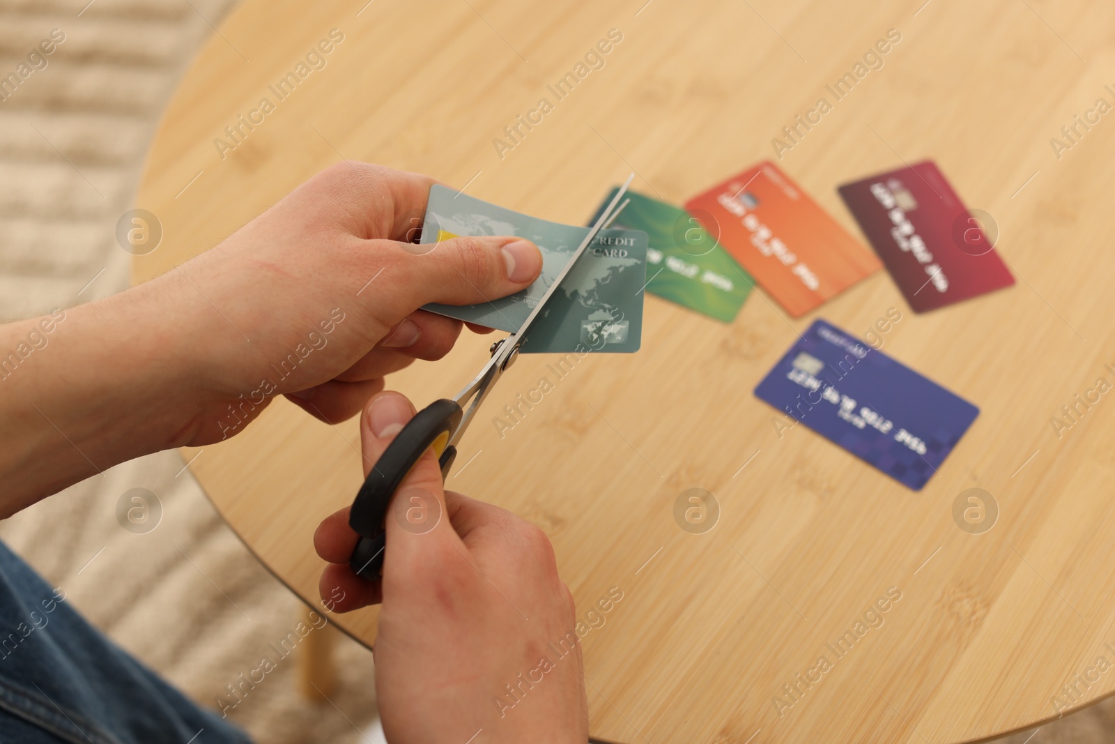 Photo of Man cutting credit card at wooden table indoors, closeup