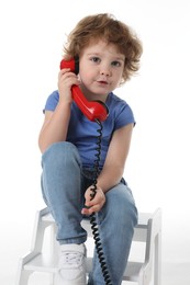 Photo of Cute little boy with telephone on step stool against white background