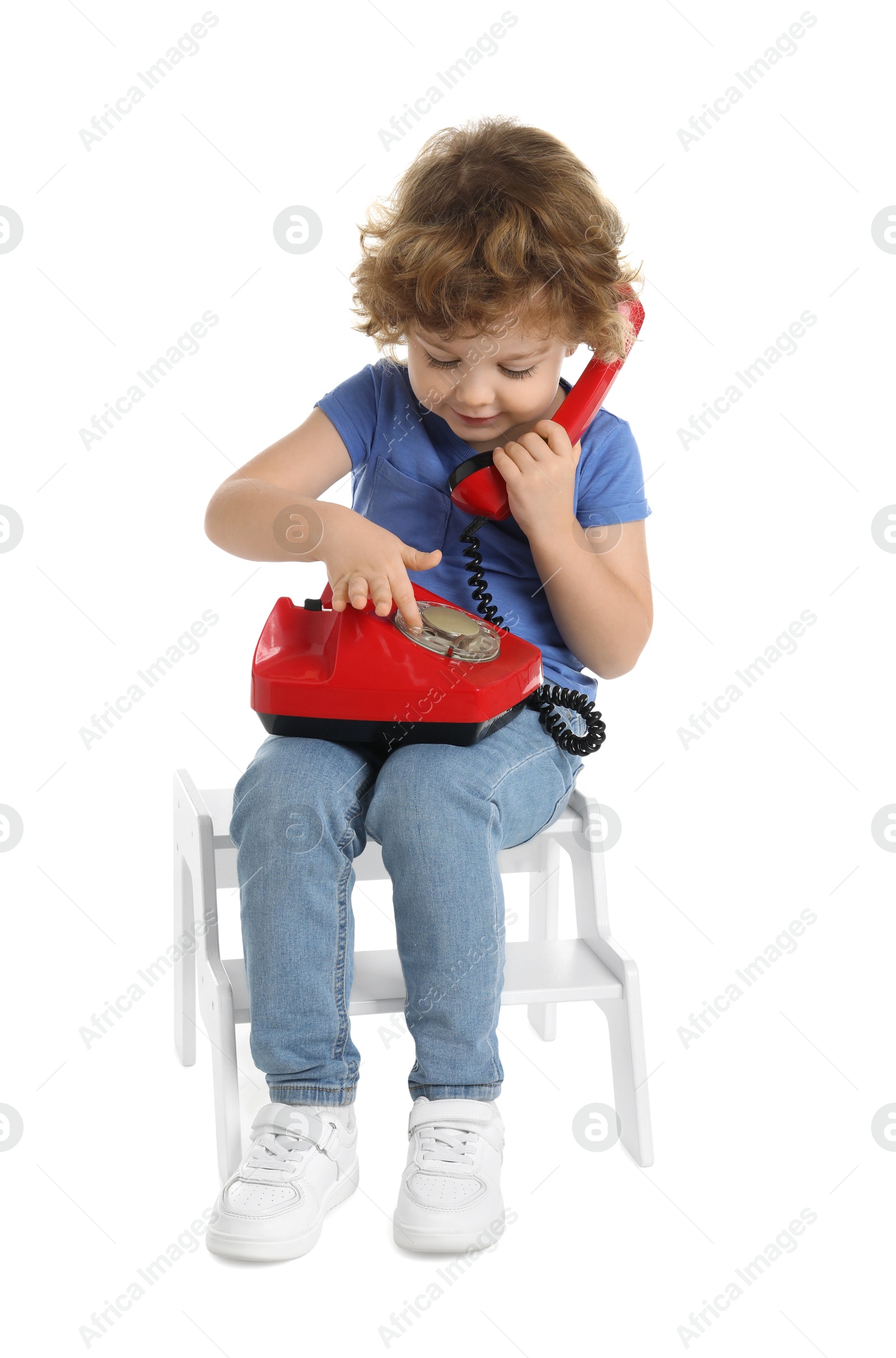 Photo of Cute little boy with telephone on step stool against white background