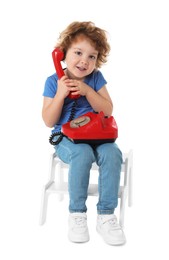 Photo of Cute little boy with telephone on step stool against white background