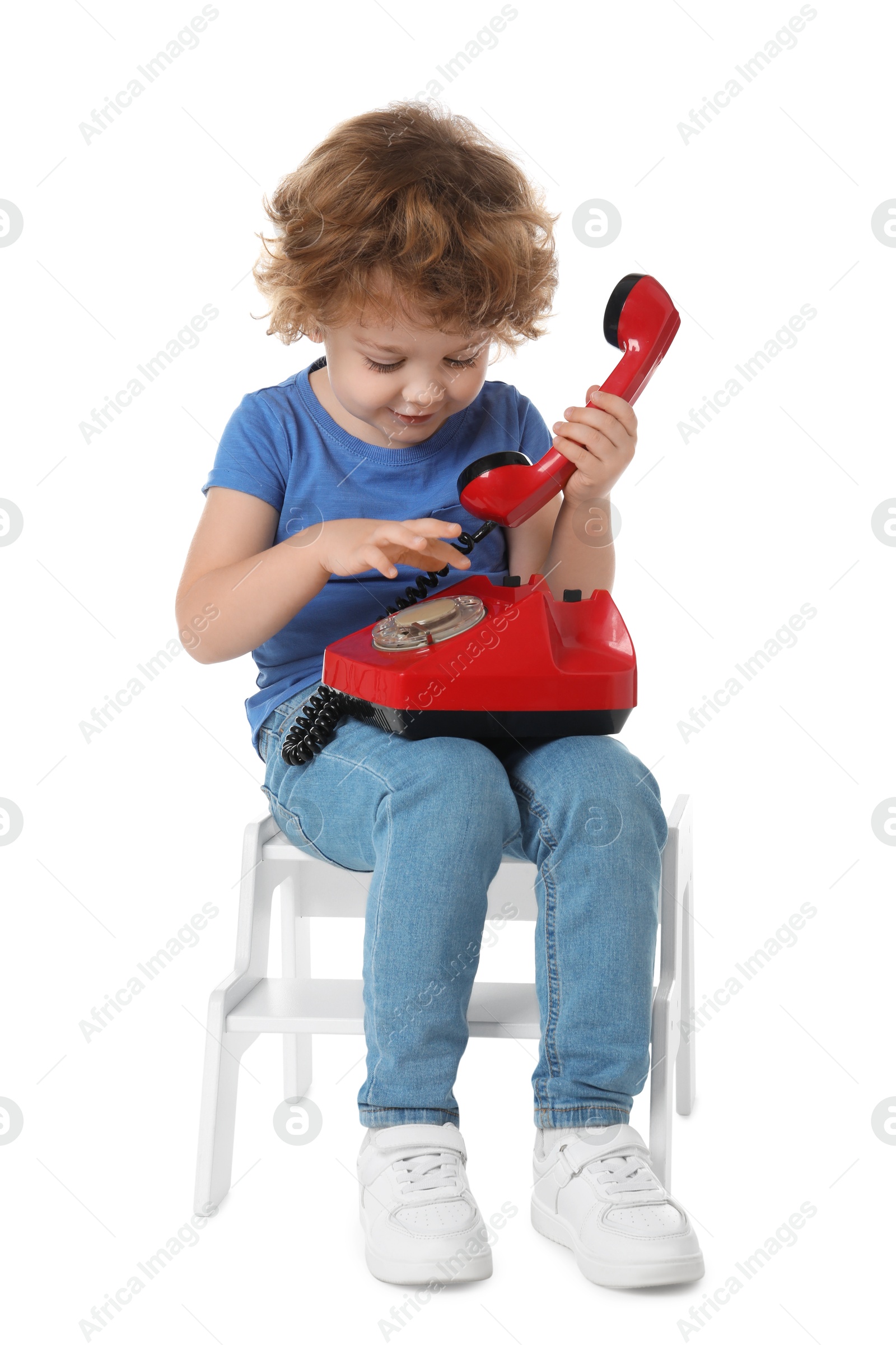 Photo of Cute little boy with telephone on step stool against white background