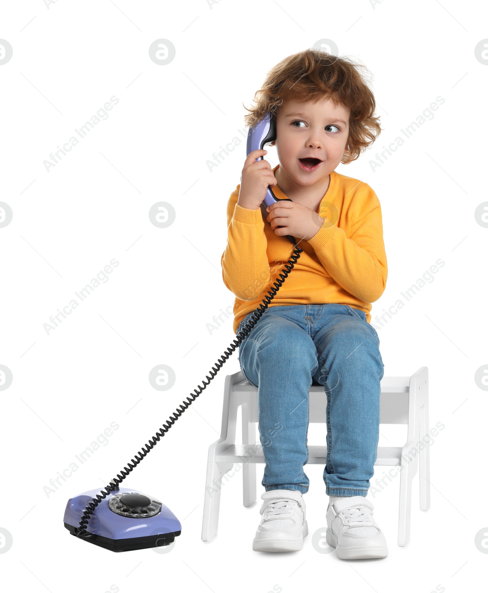 Photo of Cute little boy with telephone on step stool against white background