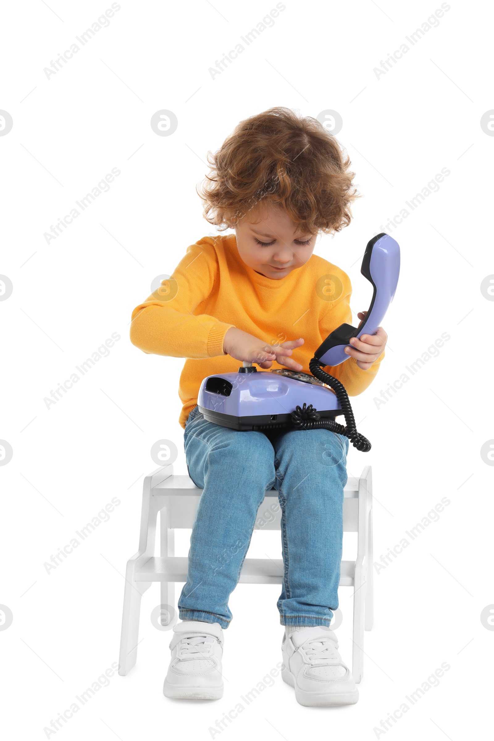 Photo of Cute little boy with telephone on step stool against white background