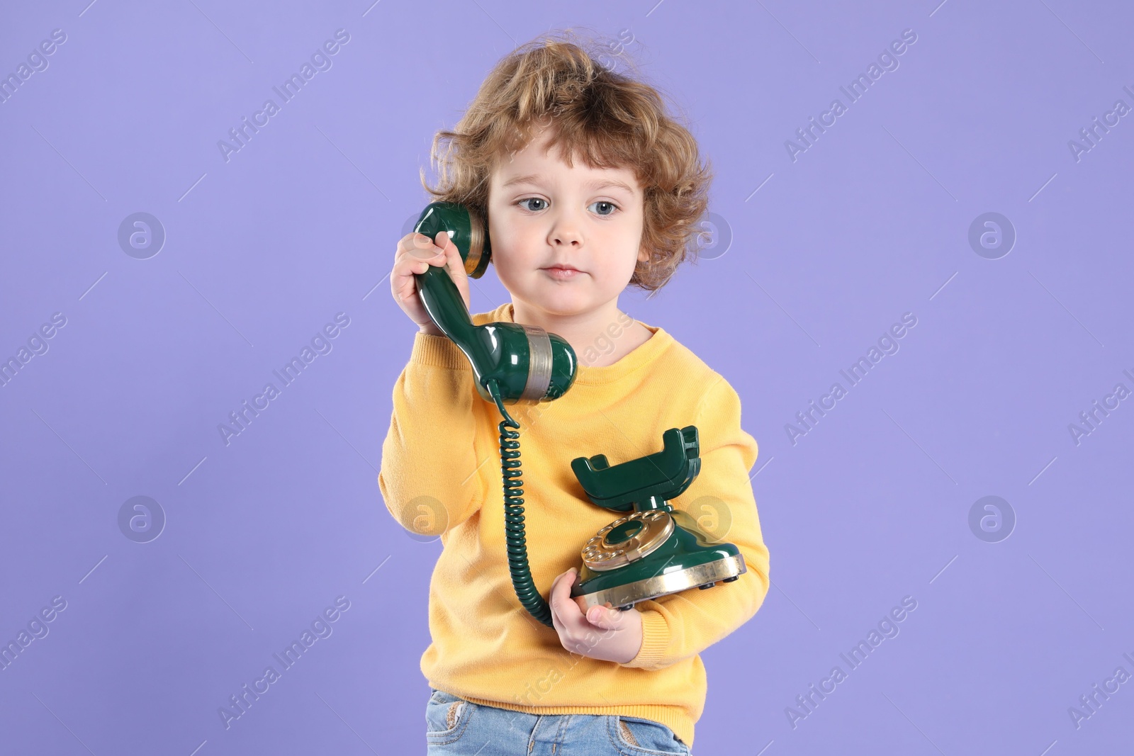 Photo of Cute little boy with old telephone on violet background