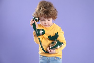 Photo of Cute little boy with old telephone on violet background