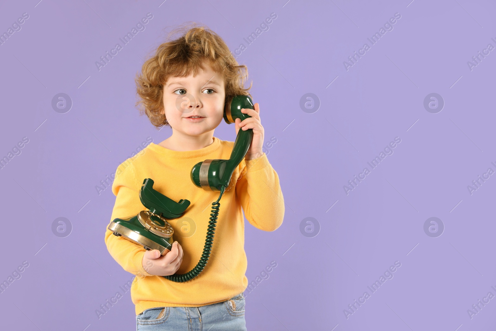 Photo of Cute little boy with old telephone on violet background, space for text