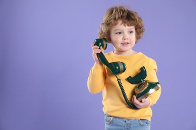 Photo of Cute little boy with old telephone on violet background, space for text