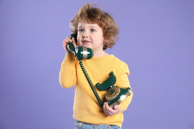 Cute little boy with old telephone on violet background