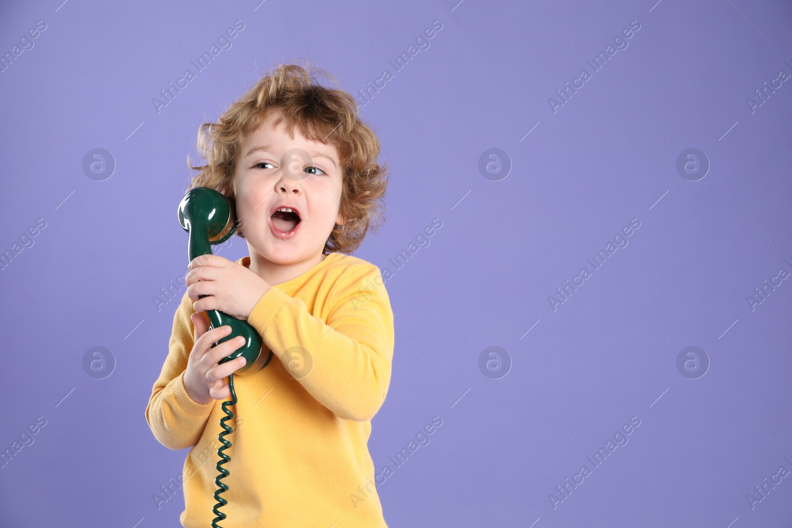 Photo of Cute little boy with telephone handset on violet background, space for text