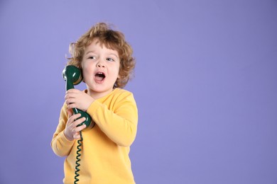 Photo of Cute little boy with telephone handset on violet background, space for text