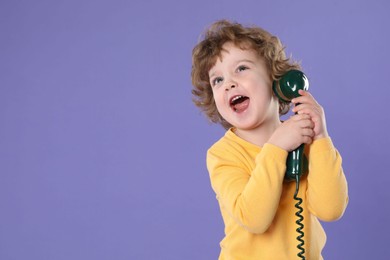 Photo of Cute little boy with telephone handset on violet background, space for text