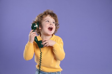 Photo of Cute little boy with telephone handset on violet background, space for text