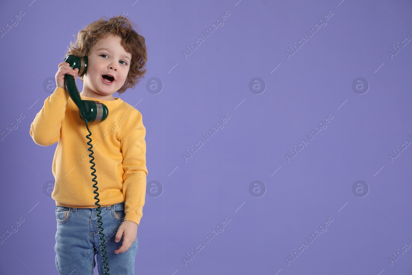 Photo of Cute little boy with telephone handset on violet background, space for text