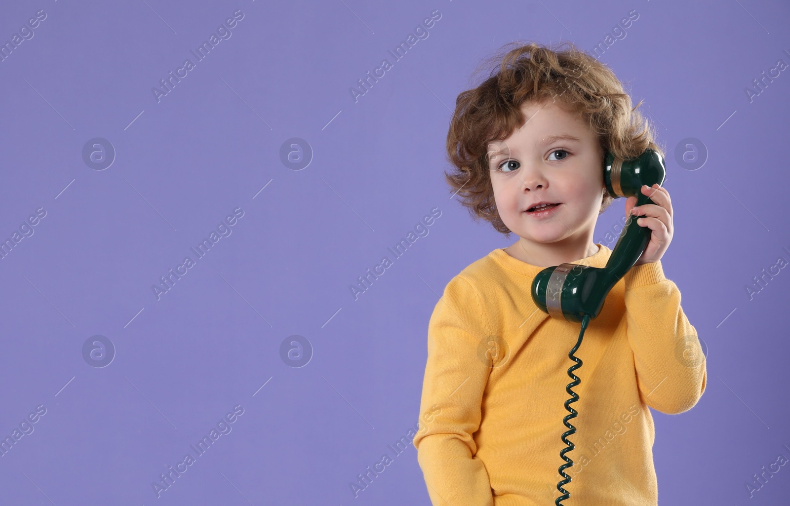 Photo of Cute little boy with telephone handset on violet background, space for text