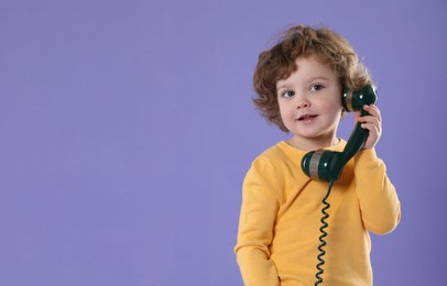 Photo of Cute little boy with telephone handset on violet background, space for text