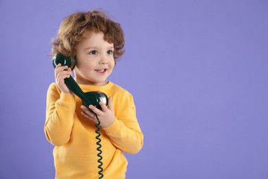 Photo of Cute little boy with telephone handset on violet background, space for text