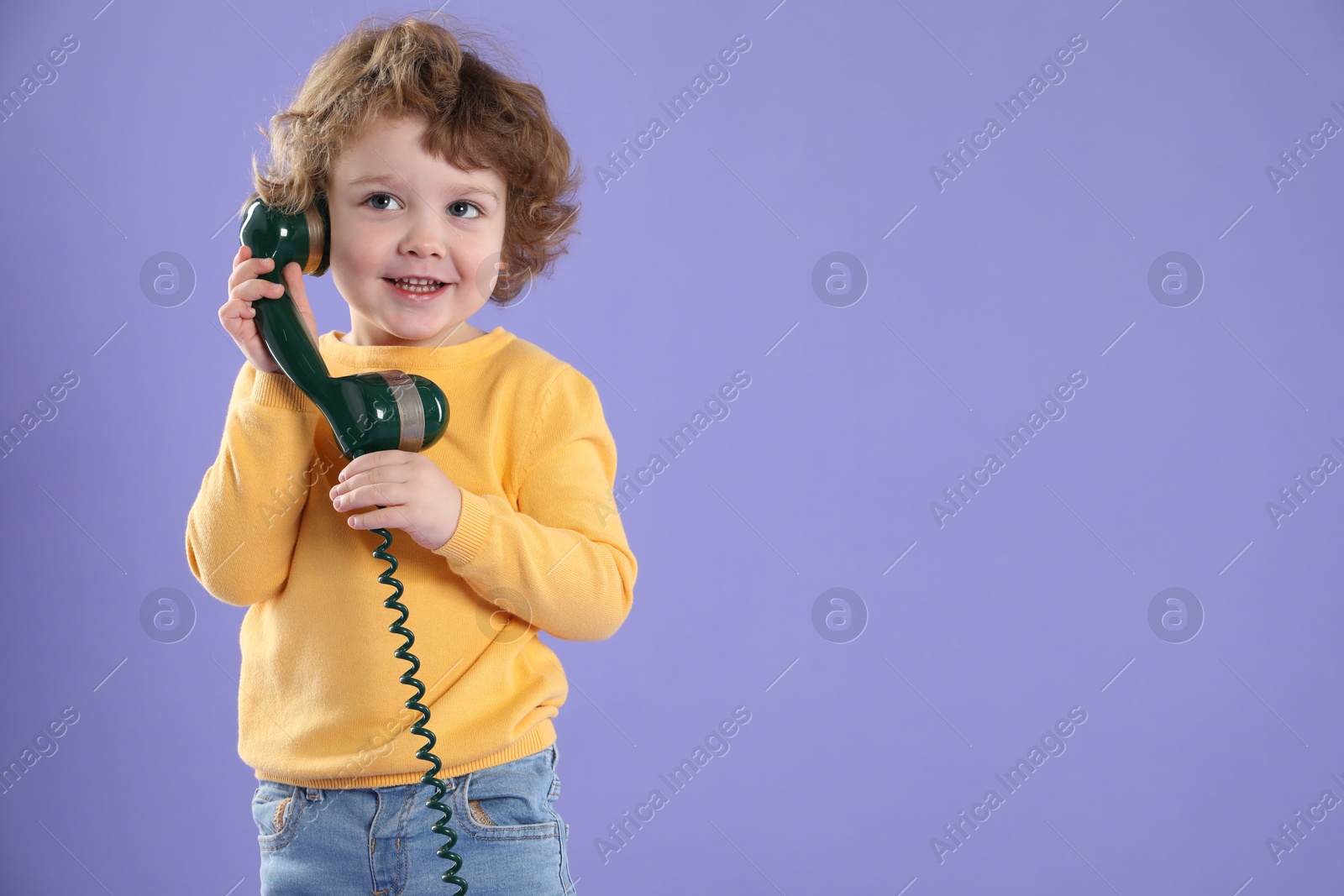 Photo of Cute little boy with telephone handset on violet background, space for text