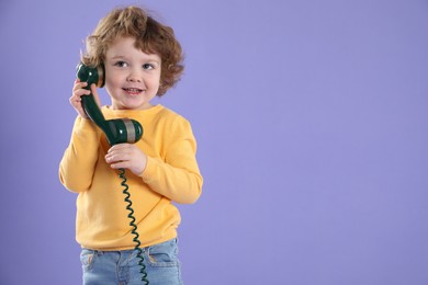 Photo of Cute little boy with telephone handset on violet background, space for text