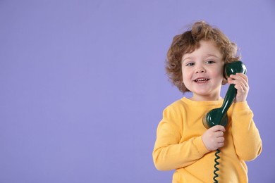 Photo of Cute little boy with telephone handset on violet background, space for text