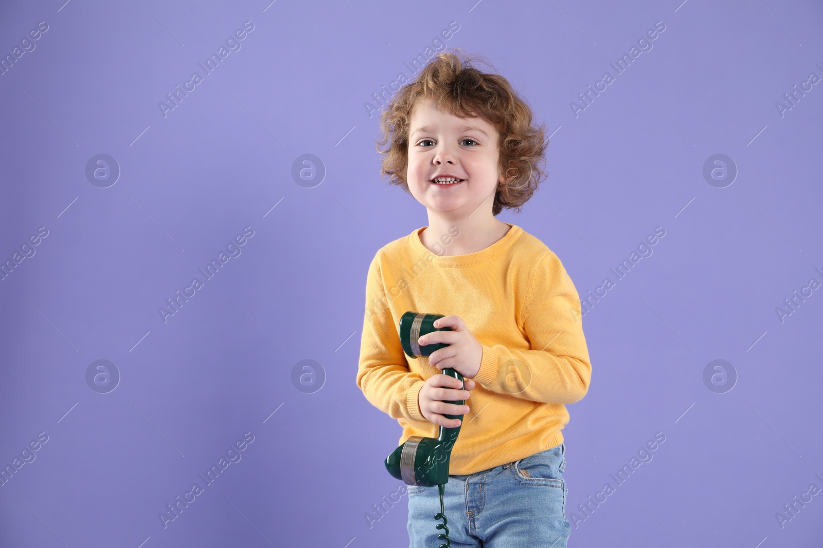 Photo of Cute little boy with telephone handset on violet background, space for text