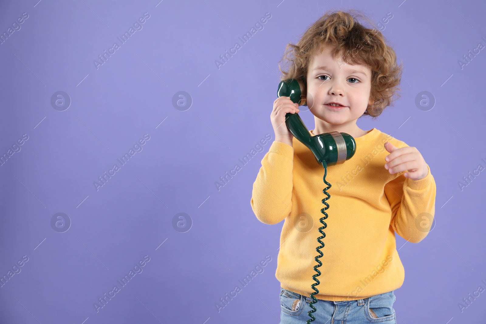 Photo of Cute little boy with telephone handset on violet background, space for text