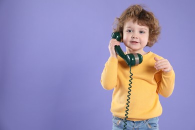 Photo of Cute little boy with telephone handset on violet background, space for text